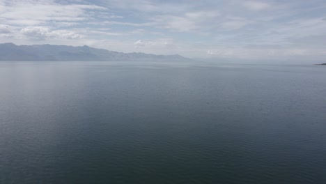 Video-Con-Un-Drone-Sobre-El-Lago-Skadar-En-Albania,-Plano-Frontal-Descriptivo-Ascendiendo-Desde-El-Agua-Para-Alcanzar-Altura,-Con-El-Horizonte-De-Las-Montañas-De-Montenegro