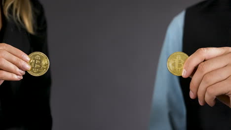 detail of male and female hand holding two gold bitcoin coins,close up