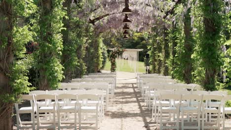 Sillas-Blancas-En-Las-Filas-Antes-Del-Altar-De-La-Boda---Ceremonia-De-Boda-En-Un-Hermoso-Jardín---Enfoque