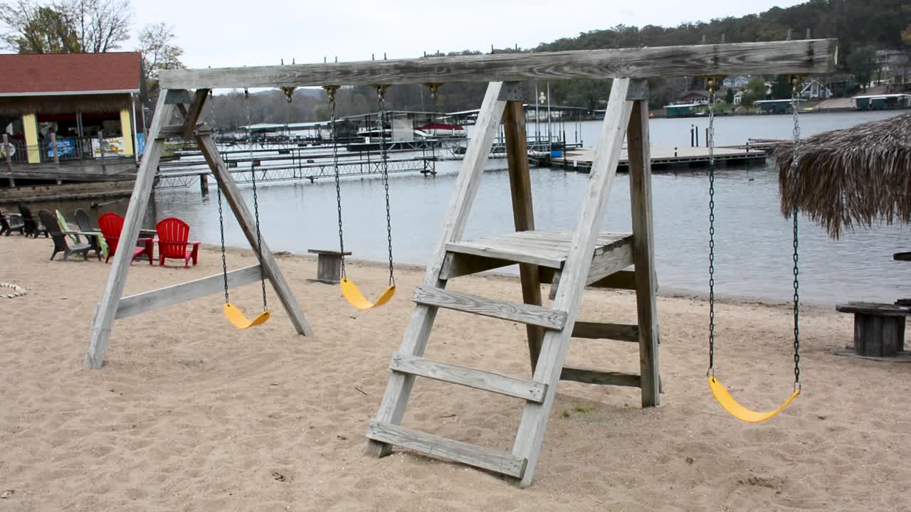 columpios amarillos vacíos balanceándose lentamente con el viento en un parque infantil en la playa en un lago