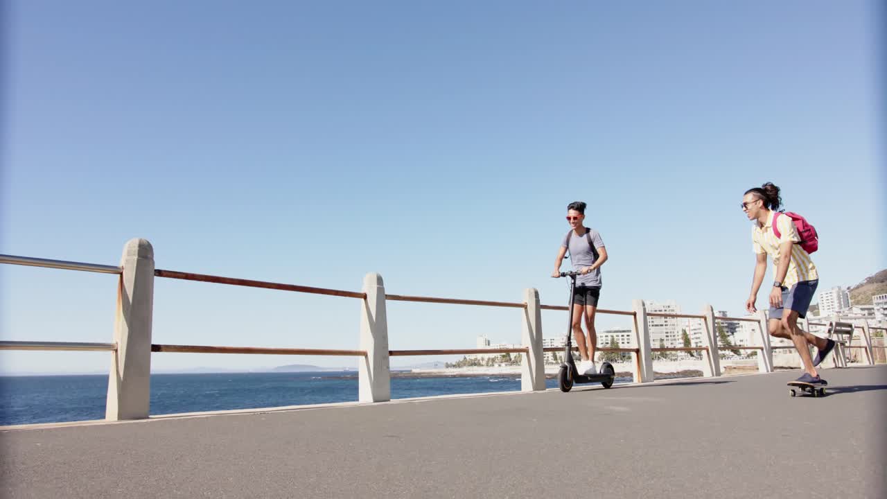 해변의 산책로에서 스쿠터를 사용하는 행복한 다양한 동성애 남성 커플, 슬로우 모션