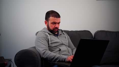 serious middle eastern male using laptop on sofa in living room