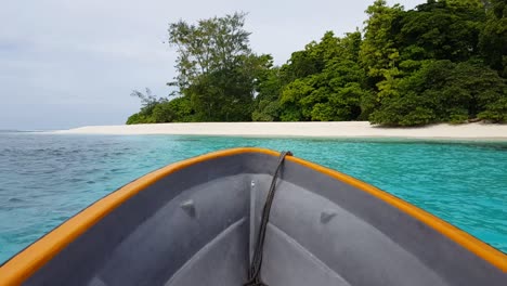 bow of small boat traveling towards a remote tropical island with white sandy beach and turquoise ocean water in solomon islands, south pacific