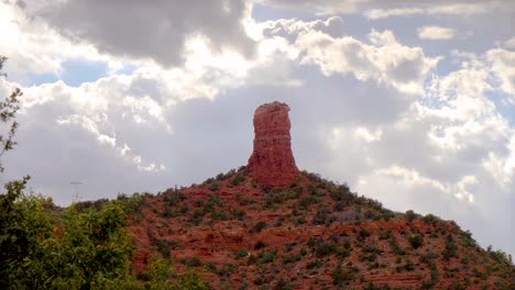 panning view of majestic glowing clouds behind a chimney formation of red rock in sedona, arizona