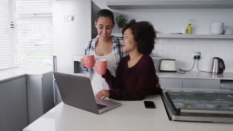 pareja de lesbianas tomando café y usando una computadora portátil en la cocina