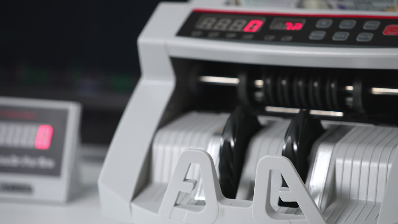 Cash counting machine switched on and the rollers begin to rotate. A wad of hundred dollar notes are placed into machine to be counted. Close up.