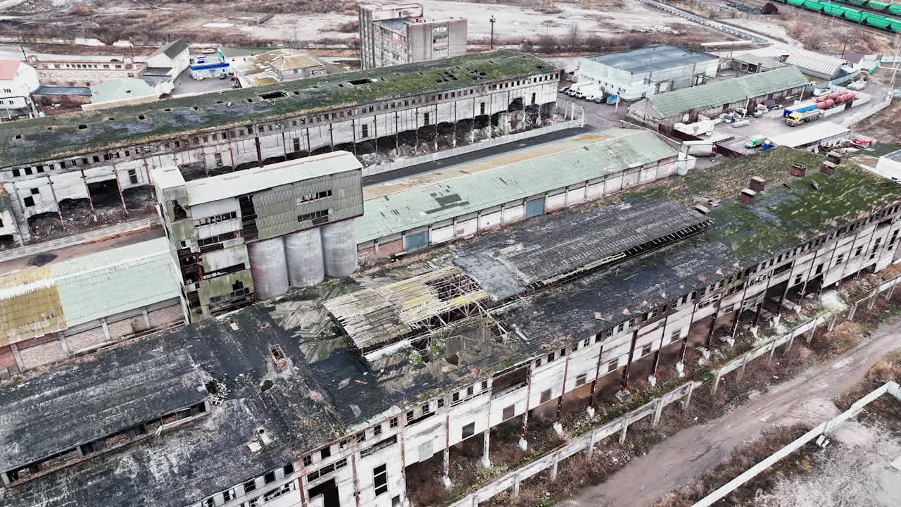 Neglected locality of a past time plant. Abandoned ruins of warehouses with broken walls, windows and roofs. Aerial view.
