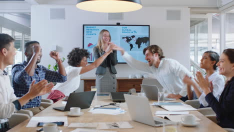 Grupo-De-Empresarios-Celebrando-En-Una-Reunión-De-La-Sala-De-Juntas-Con-Una-Mujer-Líder-Del-Equipo-Feliz-Compartiendo-Un-Informe-Financiero-Exitoso-Aplaudiendo-Y-Aplaudiendo-En-La-Oficina