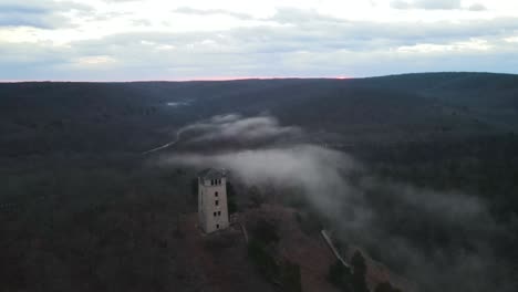 Mittelalterlicher-Burgwachturm-In-Mystischer-Nebellandschaft,-Luftaufnahme