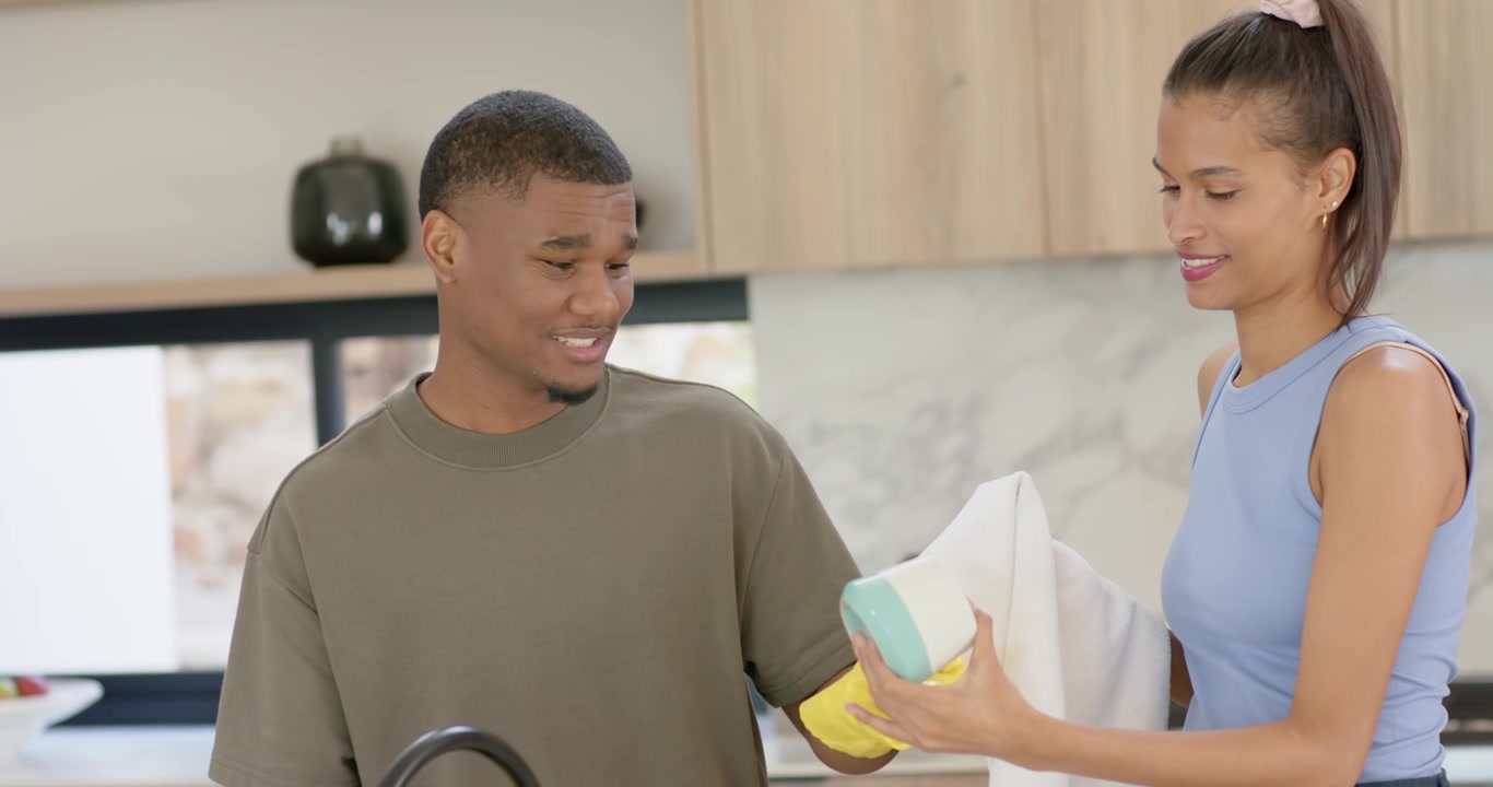 African American couple exchanging sponge while man wearing yellow glove offering container at sink