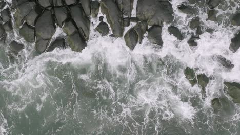 slow motion aerial overhead top down footage of ocean waves crashing into rocks that are on the coast