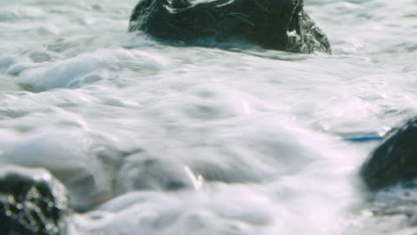 Stunning-low-level-shot-of-a-wave-washing-over-plastic-rubbish-on-a-pebbly-beach