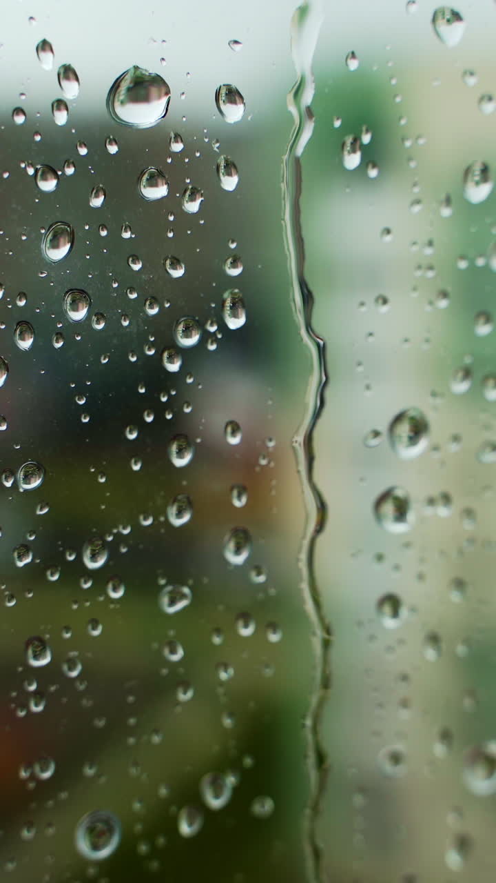 Water droplets background. Rain drops on a window pane. Water drop falling down on the window glass in rainy weather. Close-up. Vertical video