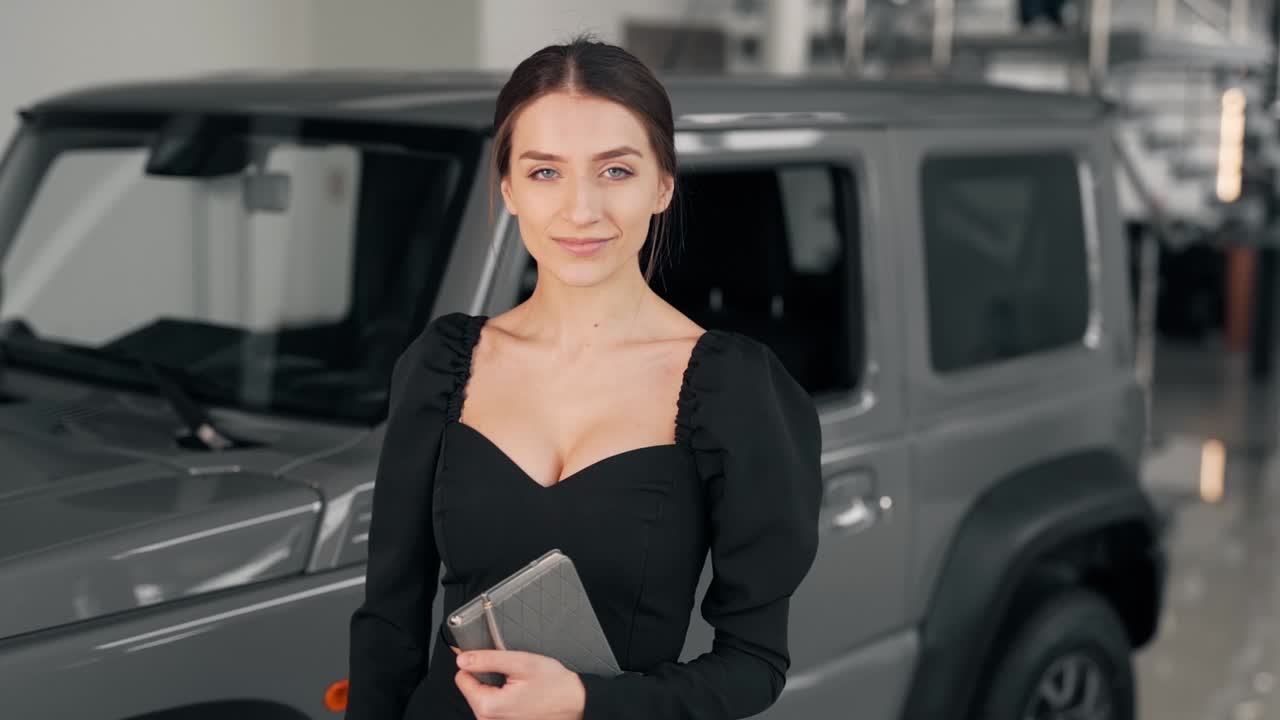 Bela jovem mulher de terno olha para a câmera e sorri com um carro ao fundo