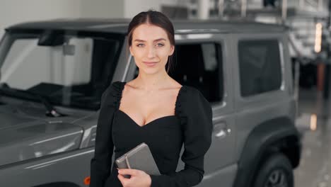 beautiful young woman in a business suit looks at the camera and smiles on the background of the car