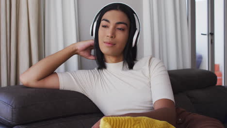 gender fluid male wearing headphones listening to music while sitting on the couch at home