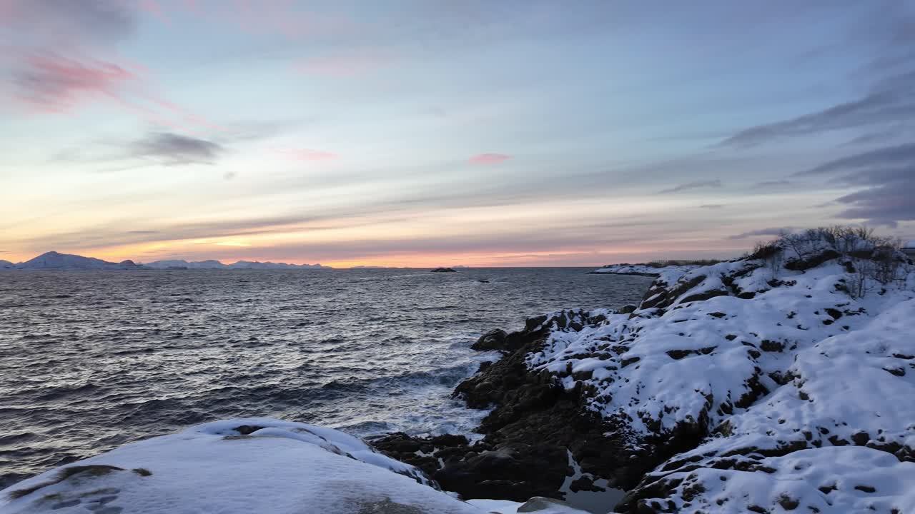 A winter sunset over a snowy coastline in Svolvær, calm and serene with icy waters