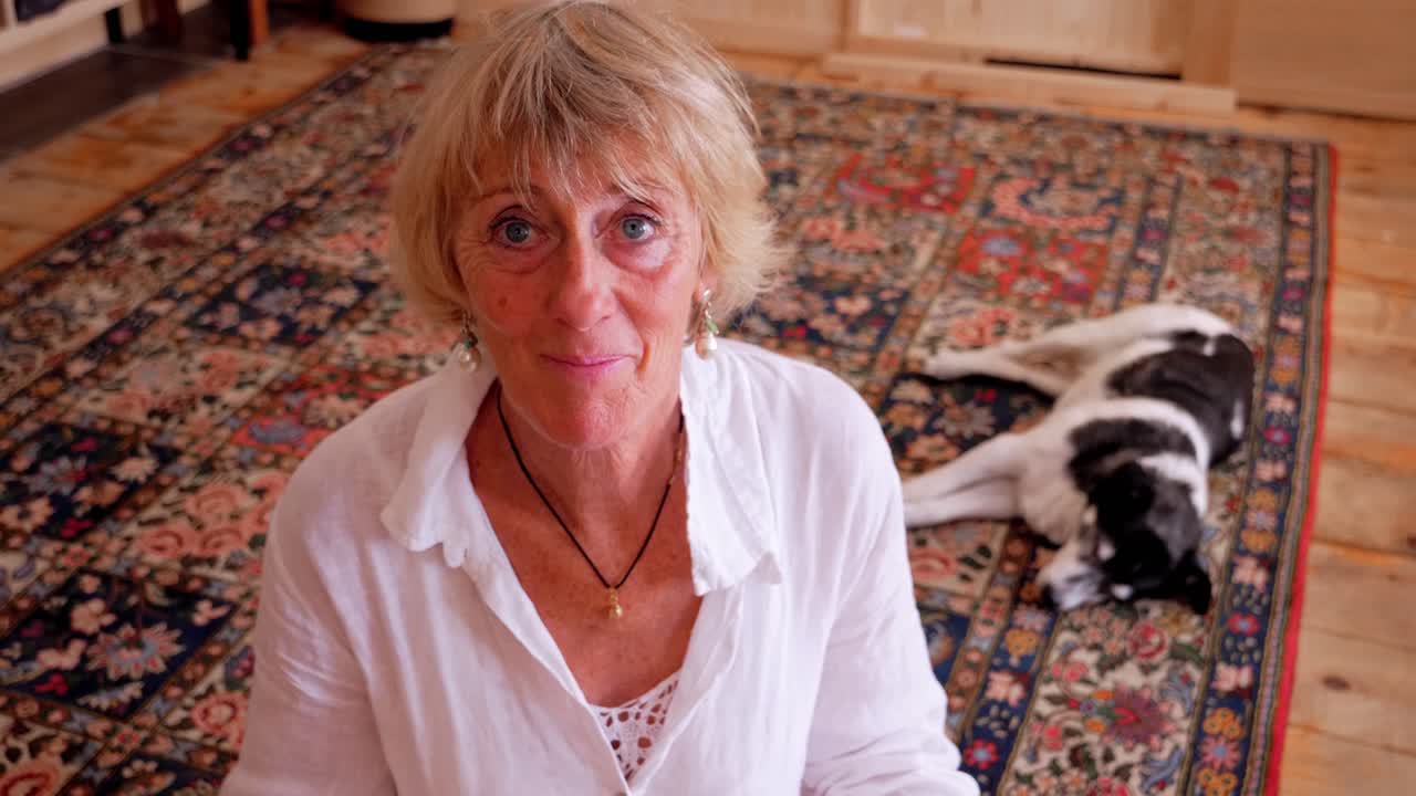 Una signora bionda seduta sul pavimento con il suo cane su un tappeto guarda da terra verso l'orizzonte