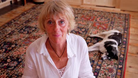 A-blonde-lady-sitting-on-the-floor-with-her-dog-on-a-rug-looks-up-from-the-ground-to-the-horizon