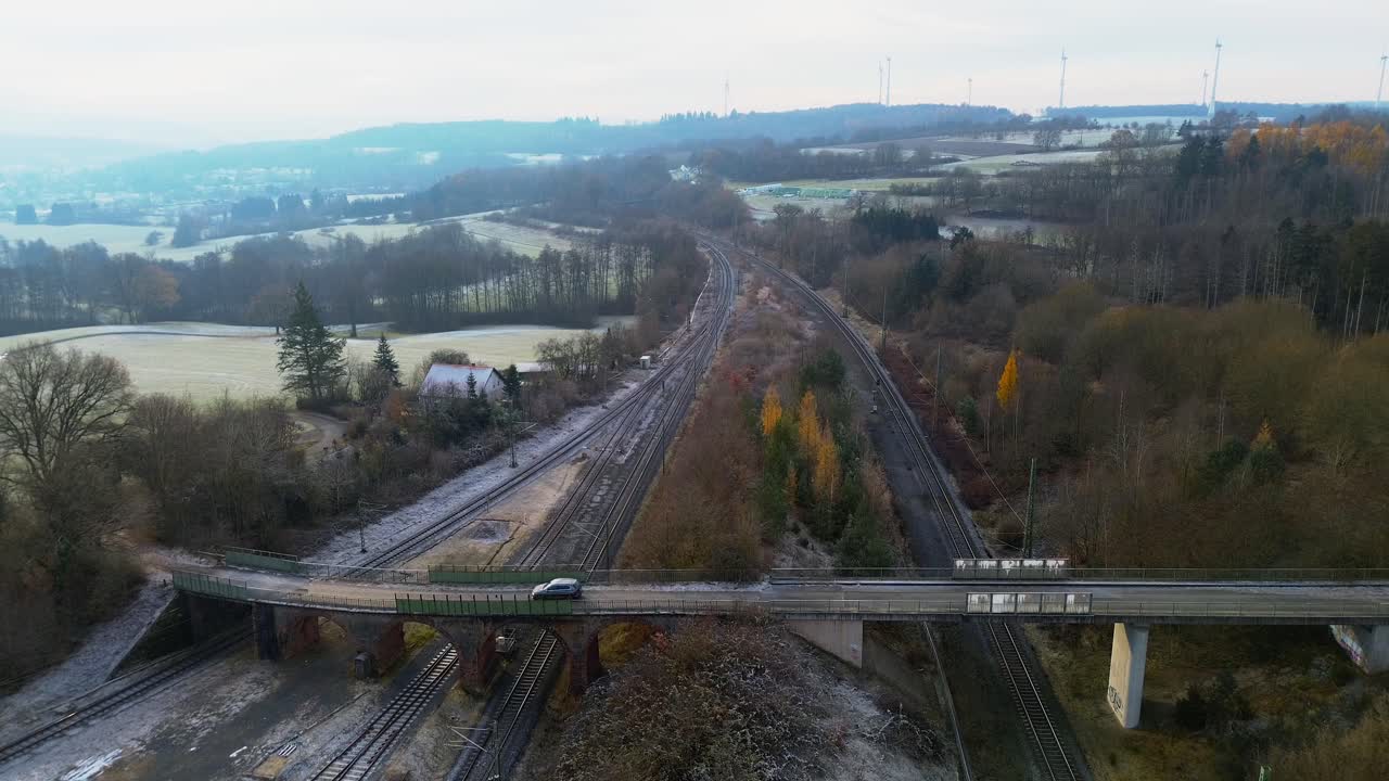 Aerial view of road bridge crossing multiple frosty railway tracks in a rural winter landscape