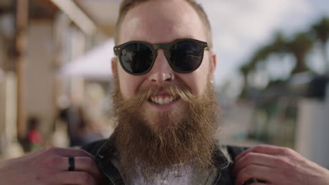 close up portrait of bearded hipster man wearing sunglasses smiling confident on beachfront