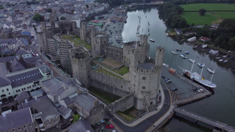 Ancient-Caernarfon-castle-Welsh-harbour-town-aerial-view-medieval-waterfront-landmark-right-overlooking-orbit-shot