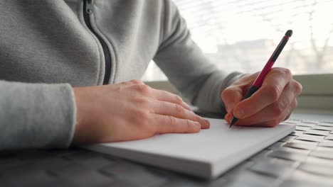 left-handed man writing on paper next to a window