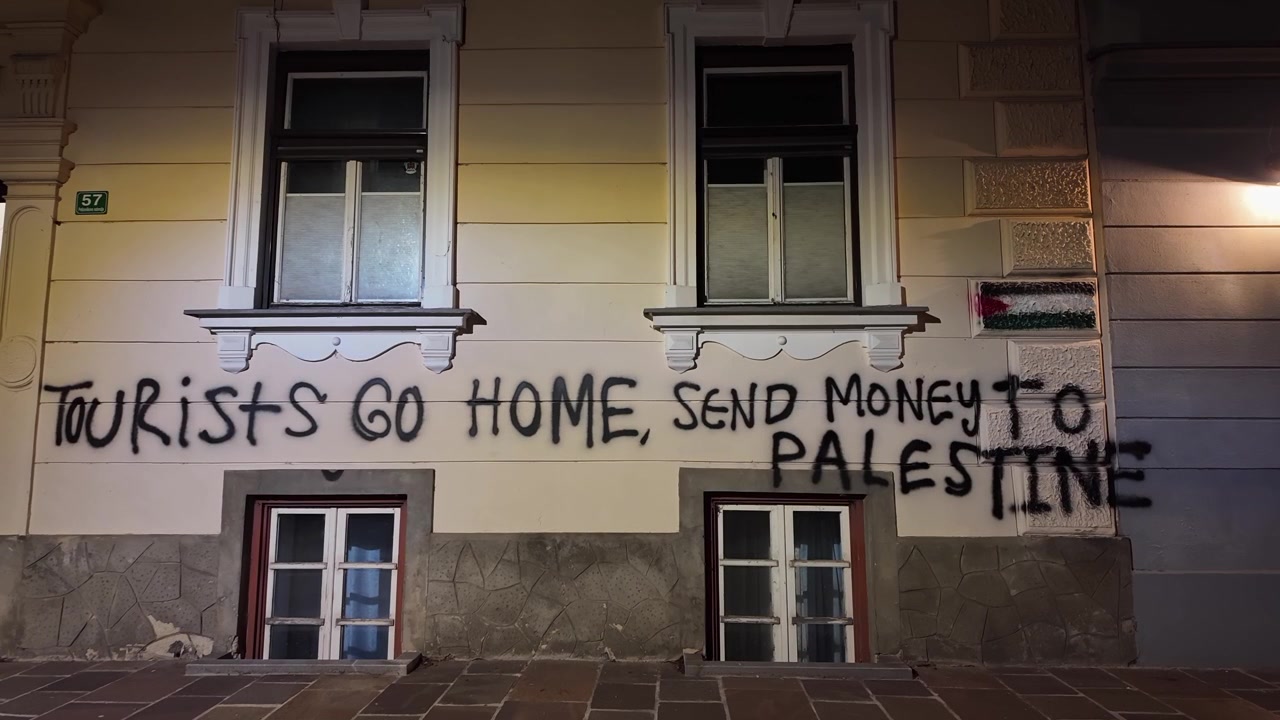 Nel centro di Lubiana, graffiti con una bandiera palestinese e messaggi politici coprono la facciata di un edificio residenziale di notte in una vivace scena di strada urbana