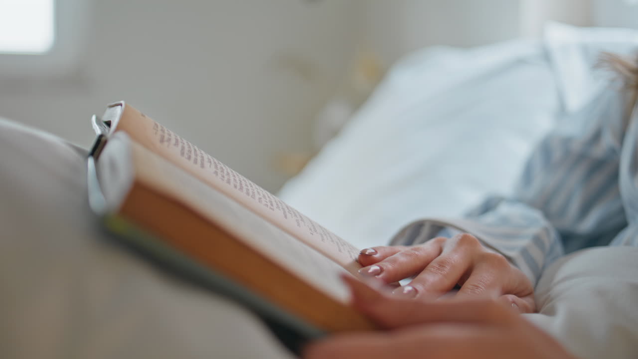 Closeup hands turning pages novel in cozy apartment bedroom. Woman reading book