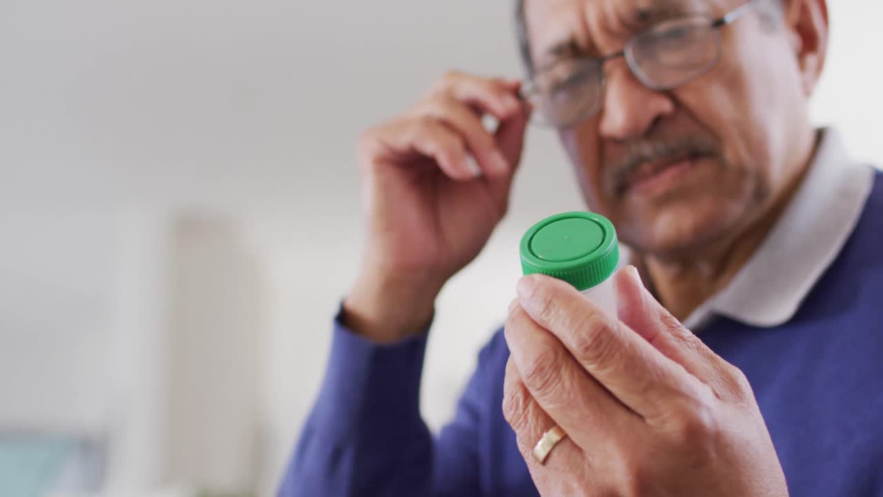 video de un hombre biracial mayor serio mirando una botella de píldoras en casa