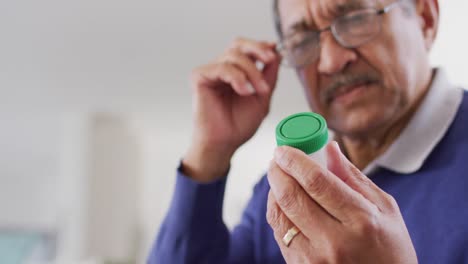 Video-of-serious-senior-biracial-man-looking-at-bottle-of-pills-at-home