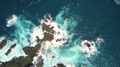 aerial top down shot of coral rocks hitting by sea waves during sunny day in yogyakarta,indonesia