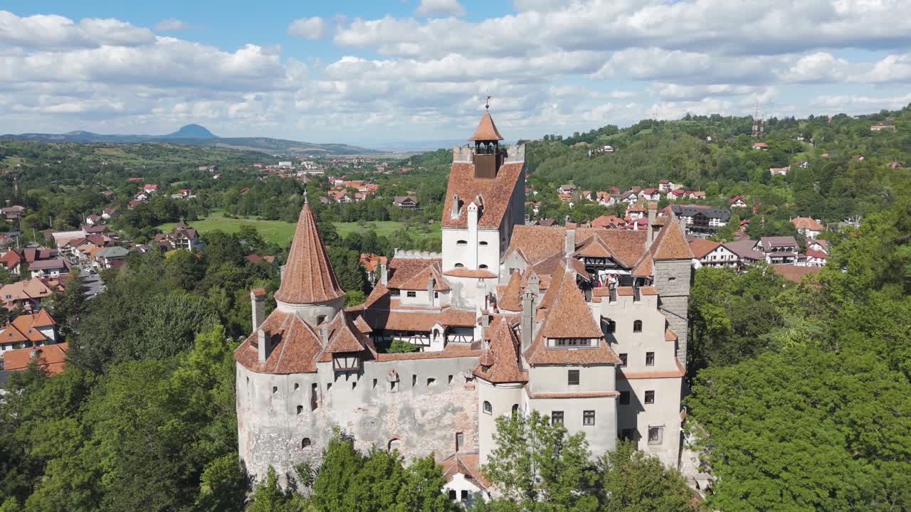 Aerial fly-in shot moving toward Bran Castle, showcasing its medieval architecture and natural surroundings