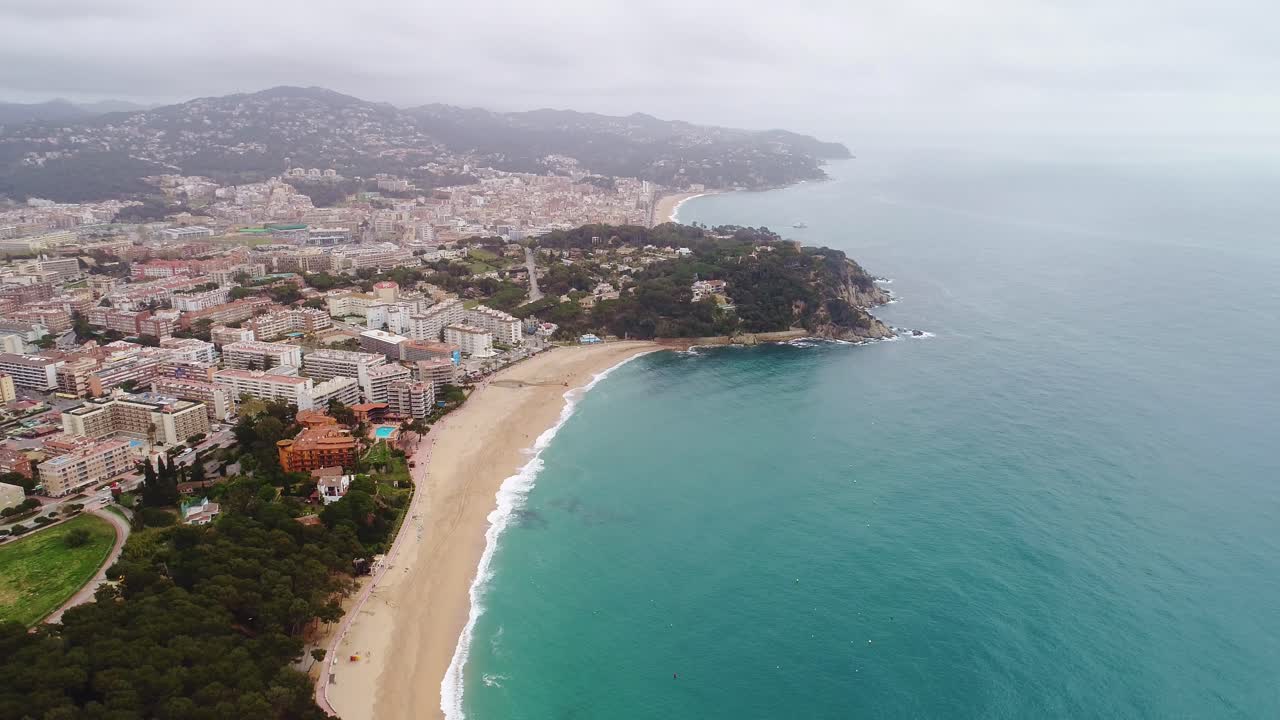 Drone captures scenic Lloret de Mar coast with mountains, buildings, blue sea