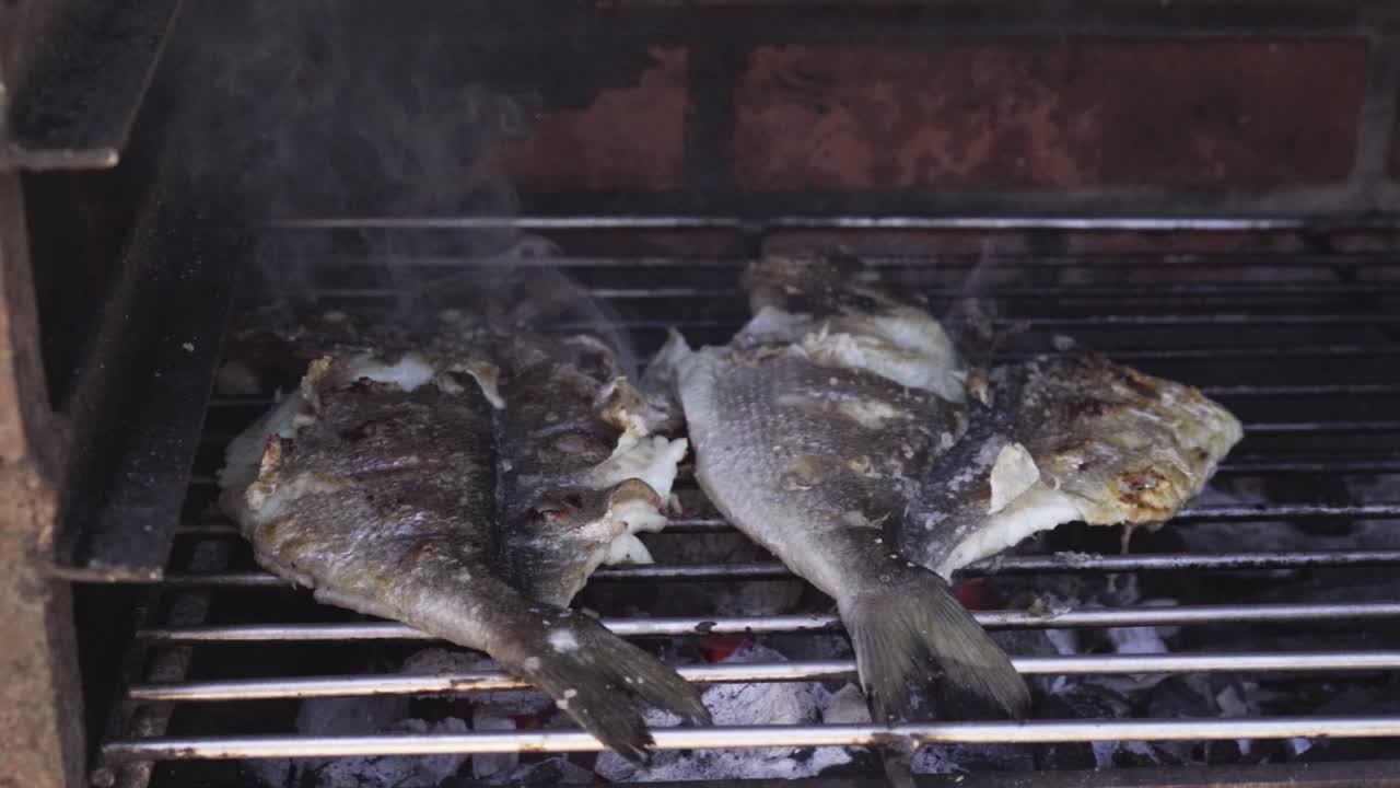 due pesci alla griglia nel carbone ardente con il fuoco sparato al rallentatore