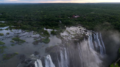 Aerial view of Victoria Falls with powerful waterfall plunging into gorge, mist rising above lush green forest, dramatic natural wonder and iconic travel destination in Africa