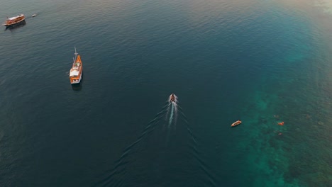 aerial view of a large wooden boat anchored offshore with a smaller speedboat approaching over deep blue water