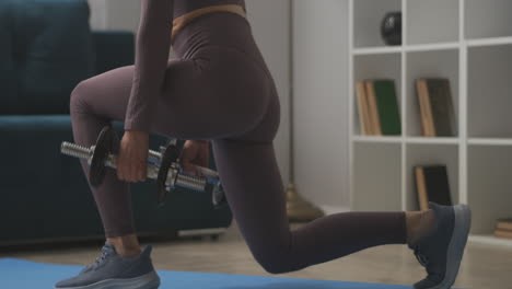 la mujer está haciendo agachadas con pesas entrenando en casa vista de cerca del cuerpo piernas delgadas nalgas y espalda fitness en la sala de estar