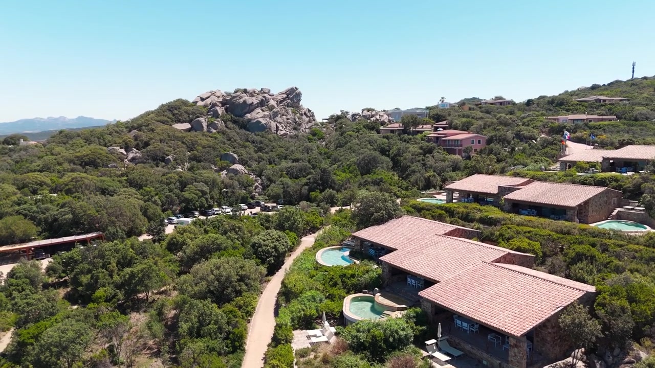 Vista aérea de villas en la ladera rodeadas de exuberante vegetación y paisaje rocoso en Cerdeña.