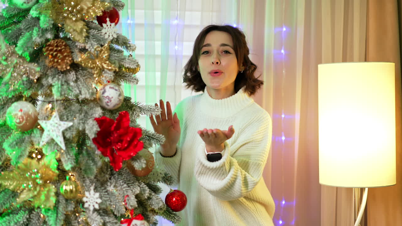 Happy woman decorating tree. A woman with curly hair is happily decorating a Christmas tree with ornaments and lights in a cozy living space