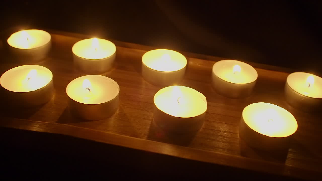 Carrellata su un vassoio di legno con candele da tè accese fino al loro spegnimento.