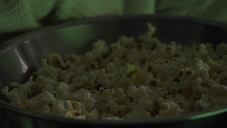 cerca de la mano de una mujer tomando palomitas de maíz del tazón