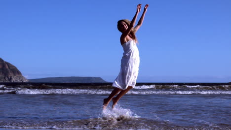 beautiful blonde leaping up in white dress on sunny day at the beach