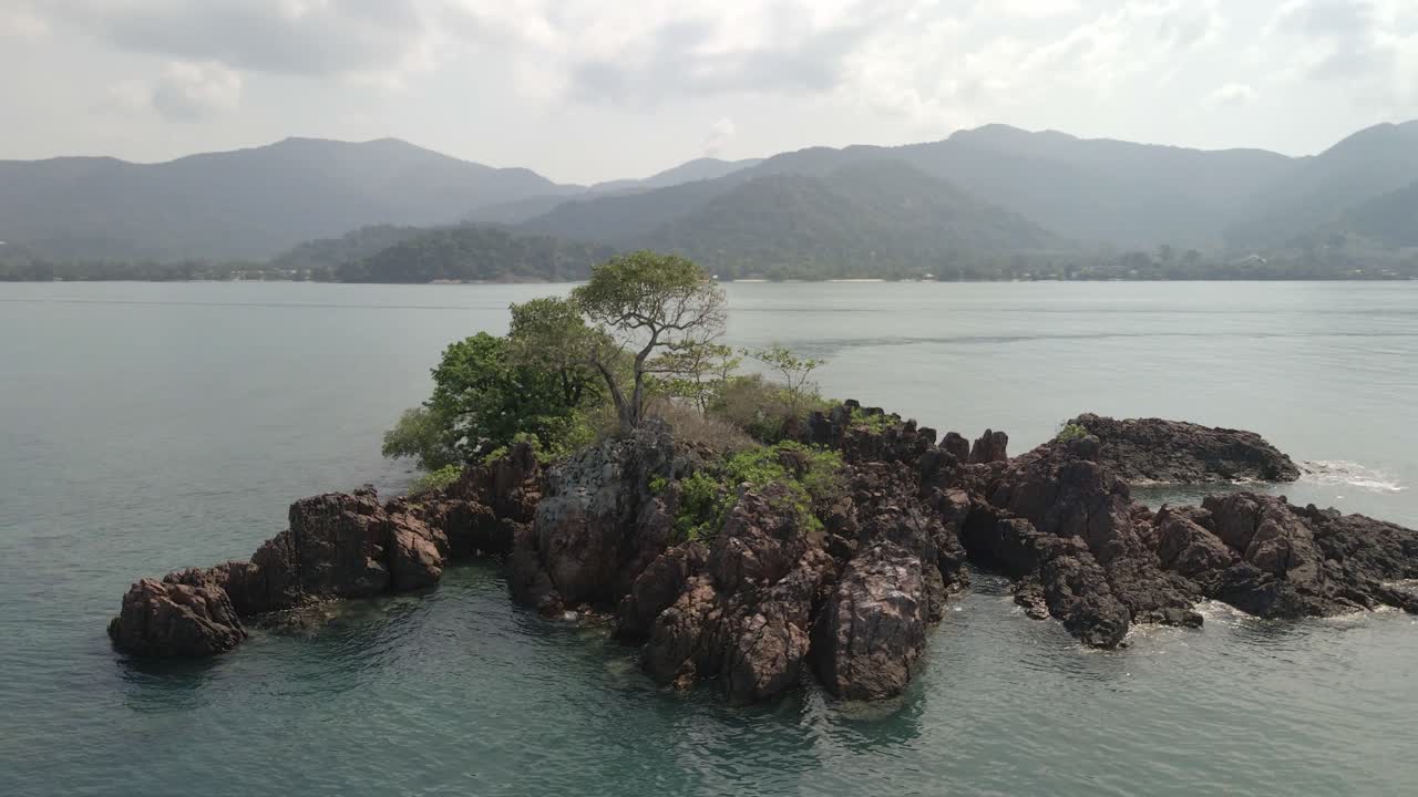 toma en órbita de drones de una pequeña isla tropical con rocas y un árbol en el golfo de tailandia con koh chang en el fondo