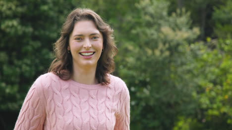 smiling woman in pink sweater enjoying nature in lush green park