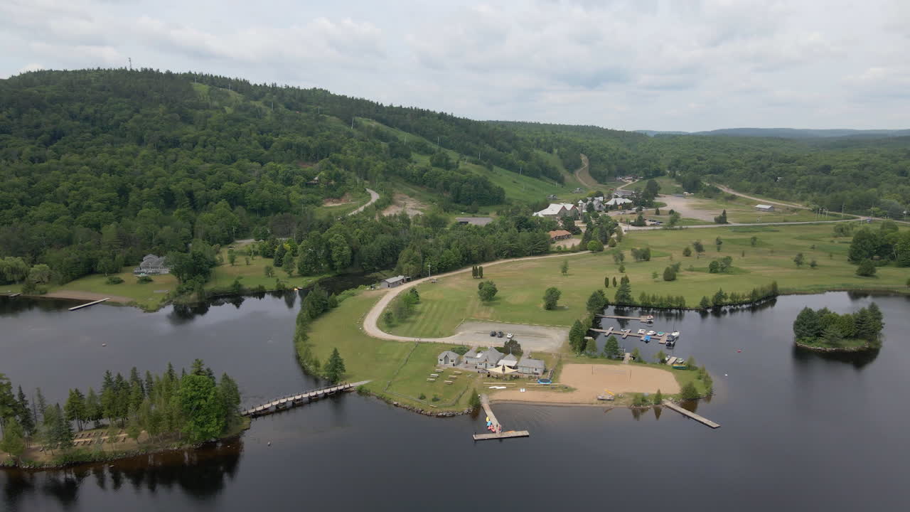 Aerial footage over lake and beach towards tree covered mountains. Calabogie ski hill, Ontario Canada