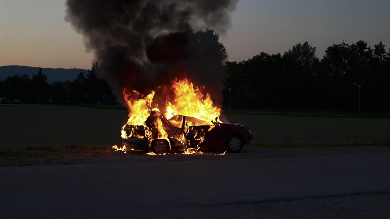 Burning car in the evening hours, long shot, from the right rear, black smoke rising, full fire - Slow Motion