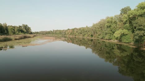 Volando-Bajo-Sobre-Un-Tranquilo-Lago-Bordeado-De-árboles-En-Un-Día-De-Finales-De-Verano