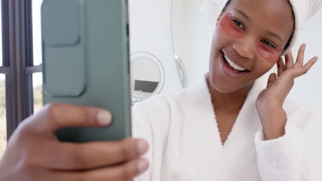 mujer biracial feliz con parches debajo de los ojos tomando una selfie con un teléfono inteligente, cámara lenta