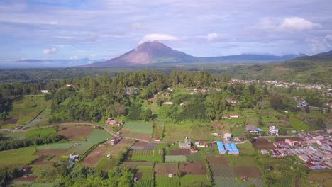 ascending stunning drone revealing shot of mount sinabung volcano and the surrounding beautiful green village in beratagi, north sumatera indonesia.